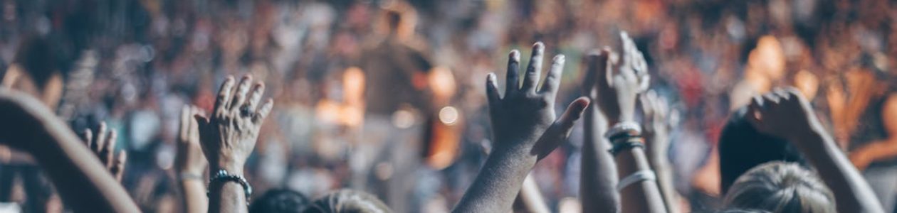 Energetic crowd at a live concert with hands raised and bright lights.